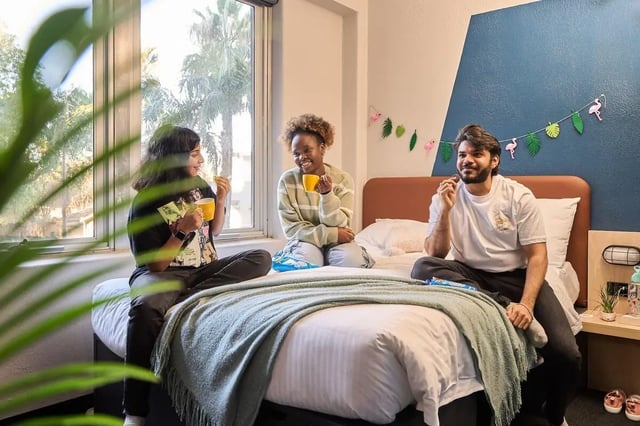 Three students sharing snacks on a bed bedroom at Campus Melbourne in Melbourne Student Accommodation