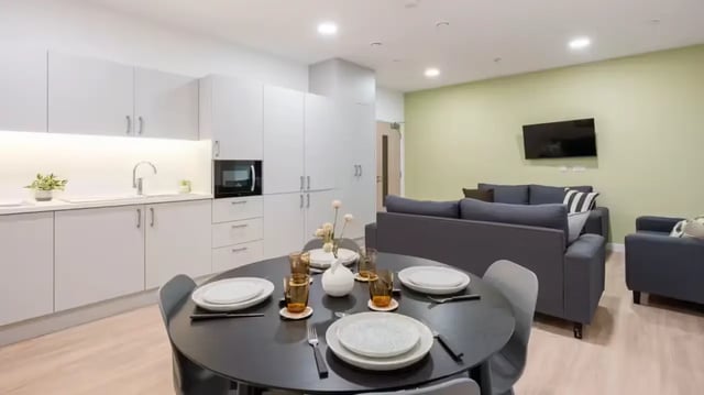 Dining table with plates, glasses, sofa, TV Living room at St Gabriels in Manchester Student Accommodation