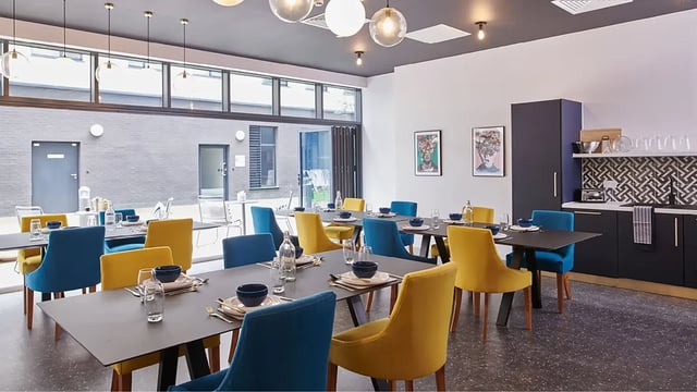 Dining tables with chairs and kitchen area communal area at Howard Gardens in Cardiff Student Accommodation