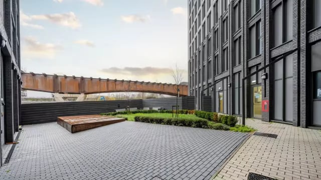 Paved courtyard with garden benches and rusty bridge exterior at Compass in Birmingham Student Accommodation