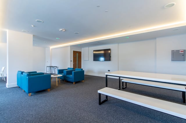 Blue chairs TV and long white tables Living Room at AXO Seven Sisters in London Student Accommodation