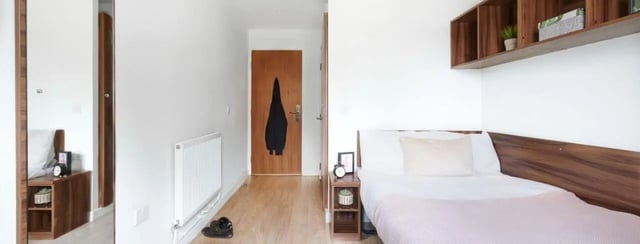 Bed clock plant wooden shelves doorway bedroom at The Printworks in Exeter Student Accommodation