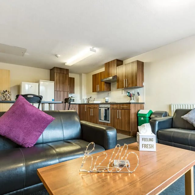 Black couches purple pillow kitchen area living room at The Pinnacles in Sheffield Student Accommodation