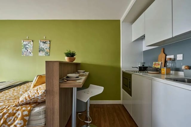 Bed with yellow pillows and kitchen area studio at Selly Oak Court in Birmingham Student Accommodation