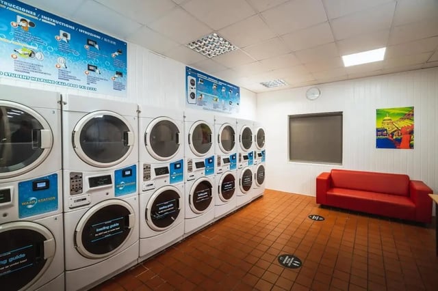 Rows of washing machines red sofa and artwork Laundry Room at The Junxion Lincoln in Lincoln Student Accommodation