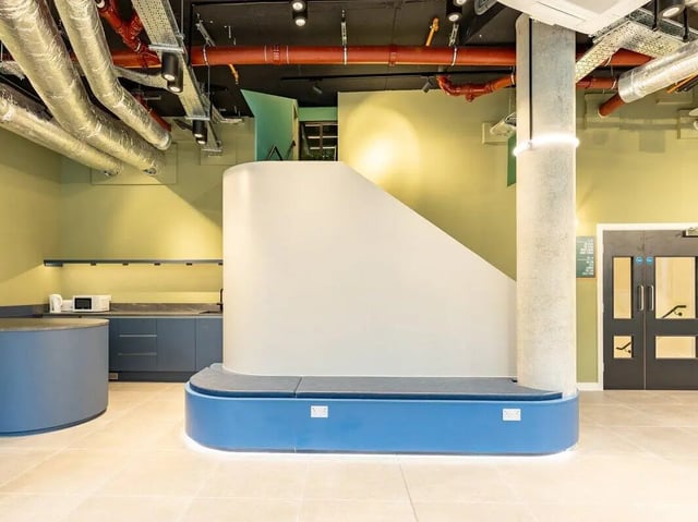 Blue bench with white wall and kitchen area Communal Area at Sheares Hall in Newcastle Upon Tyne Student Accommodation