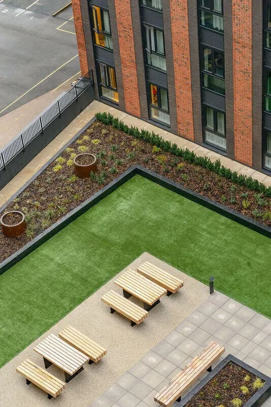 Wooden benches on artificial turf and paving exterior at True Nottingham in Nottingham Student Accommodation