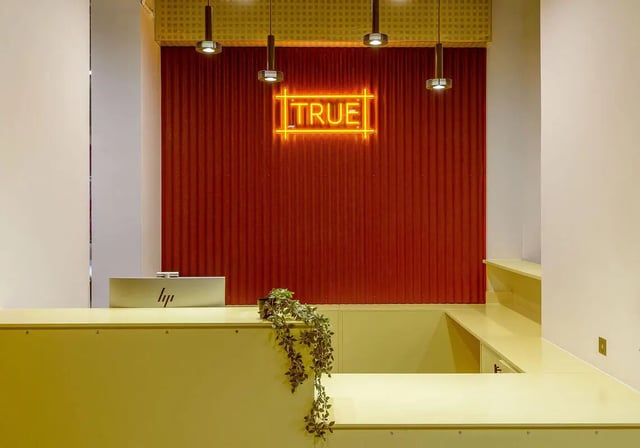 Reception desk with neon sign plant interior at True Sheffield in Sheffield Student Accommodation