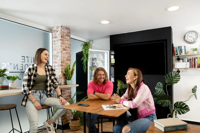 Students conversing at a table with a TV living room at The Bakery in Cardiff Student Accommodation