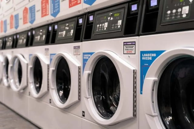 Row of washing machines with digital displays laundry room at LIV Student Belfast in Belfast Student Accommodation