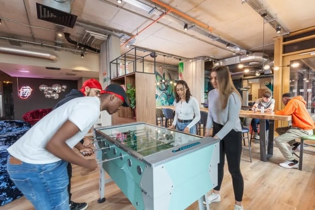 Students play foosball at tables with bar seating living area at LIV Student Sheffield in Sheffield Student Accommodation