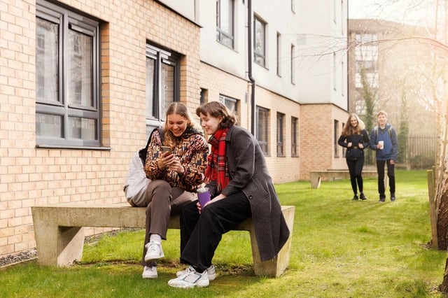 Students on bench looking at phone exterior at Murano House in Edinburgh Student Accommodation