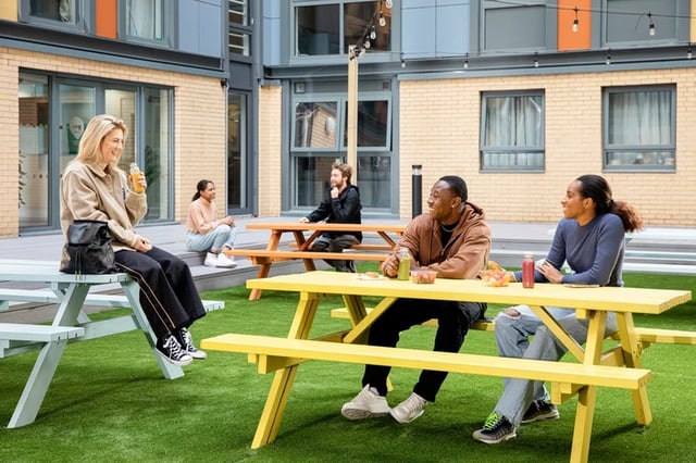 Students sitting at picnic tables exterior courtyard at Blithehale Court in London Student Accommodation