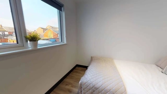 Quilted bed and plant by window bedroom at Opto village in Luton Student Accommodation