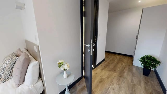 Bed with pillows small table flowers hallway interior at Opto village in Luton Student Accommodation