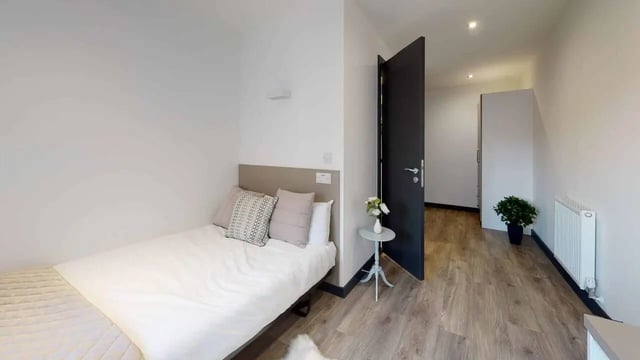 Bed pillows side table plant radiator bedroom at Opto village in Luton Student Accommodation