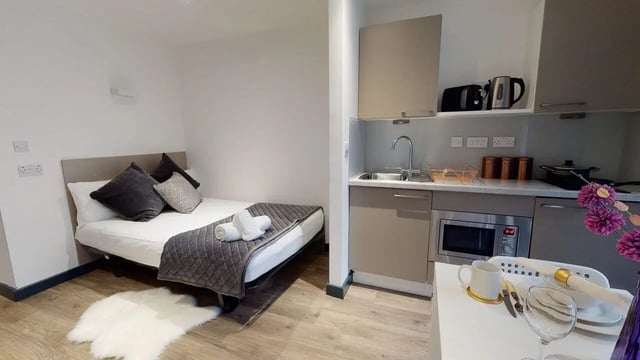 Bed with pillows kitchen area with sink Studio apartment at Opto village in Luton Student Accommodation