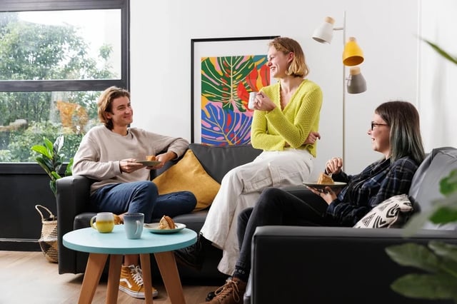 Three students chatting on sofas eating cake living room at Rosalind Franklin Halls in Portsmouth Student Accommodation
