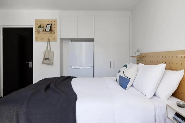 Bed with grey blanket pillows fridge and cabinets bedroom at UKO Paddington Village in Sydney Student Accommodation