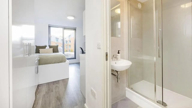 Bed desk and shower visible student room bathroom at The Cube Ealing in London Student Accommodation