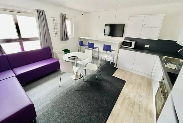 Purple sofa white table bar stools kitchen living area at Creek Court in London Student Accommodation