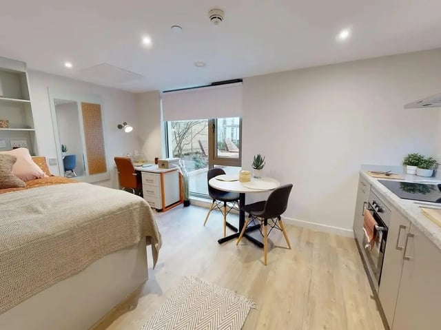 Bed desk table chairs and kitchen living room at COSMOS in Sheffield Student Accommodation