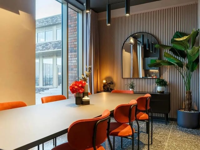 Dining table with orange chairs large plant and mirror dining area at COSMOS in Sheffield Student Accommodation