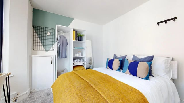 Bed with yellow blanket wardrobe and pillows bedroom at 6 Bedroom House at 18, Halsbury Road in Liverpool Student Accommodation