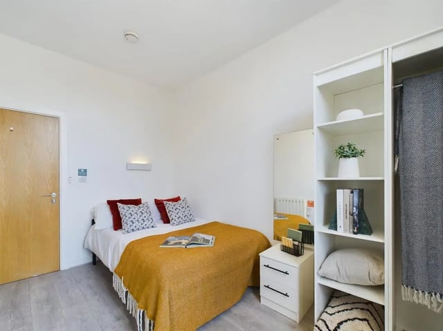 Bed with yellow blanket and pillows, white nightstand, shelves bedroom at 5 Bedroom House at Flat 4, 18, China Street in Lancaster Student Accommodation