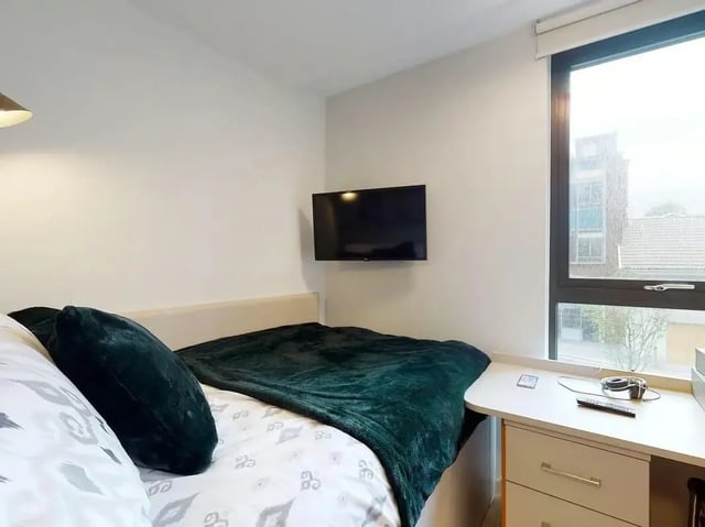 Bed with pillows blanket TV and desk Bedroom at SEREN in Swansea Student Accommodation