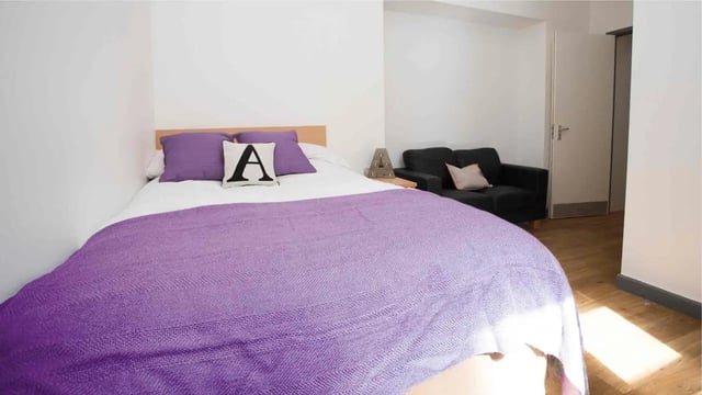 Bed with purple blanket sofa lamp and door bedroom at Alexandra Hall in Aberystwyth Student Accommodation