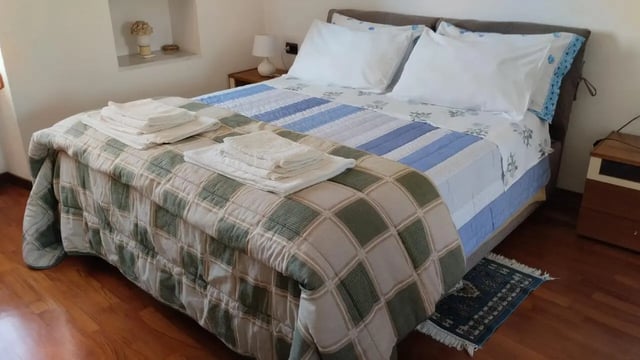 Bed with stacked towels and blue quilt bedroom at 2-bedroom house, with outdoor area in La Spezia Student Accommodation