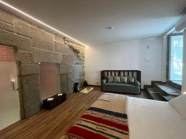 Bed sofa stone wall and wooden floor bedroom at Spacious Double Bedroom ensuite close to Barragem de Vascoveiro in Guarda Student Accommodation