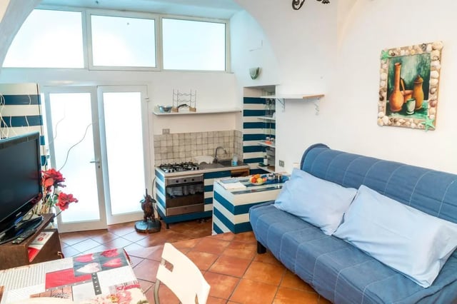 Blue sofa with pillows and kitchen area living room at Cosy double-bedroom apartment in Albenga (SV) in Albenga Student Accommodation