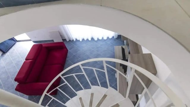 Red sofa white spiral staircase living room at Comfy Apartment close to the beach in Agrigento Student Accommodation
