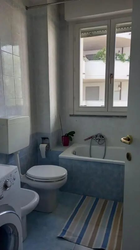 Toilet washing machine bath striped rug bathroom at Comfy 3 bedroom apartment close to University of Parma in Parma Student Accommodation