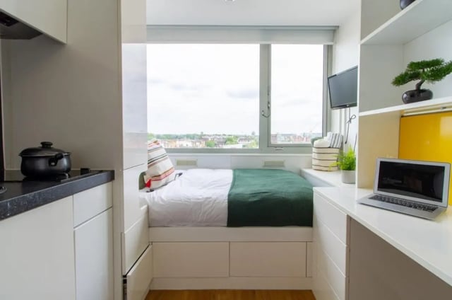 Bed with green blanket and pillows kitchen area study area bedroom at Chelsea Lightfoot Hall in London Student Accommodation