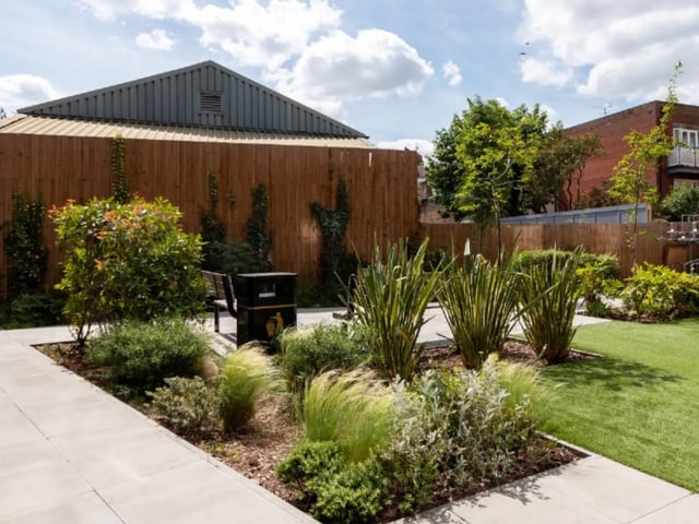 Bench trash bin and green plants garden exterior at AXO Kingston in Kingston Upon Thames Student Accommodation