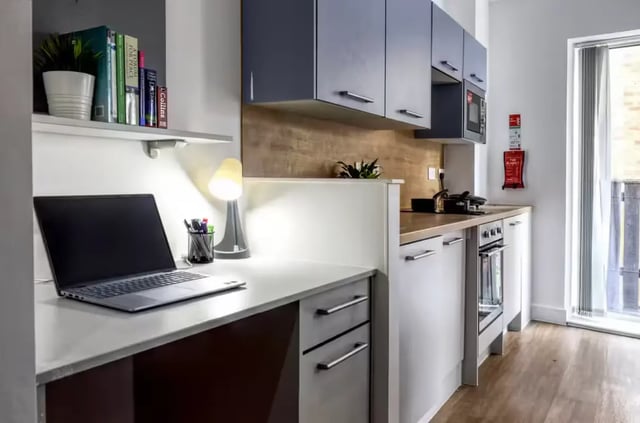 Desk with laptop, lamp, books, kitchen. at Orbital in Nottingham Student Accommodation