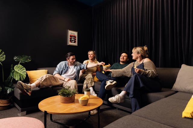 Students relaxing on sectional couch eating chips living room at Byron Central in Newcastle Upon Tyne Student Accommodation