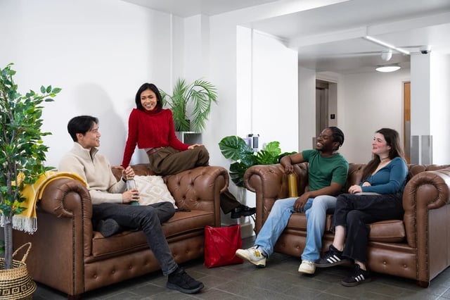 Four friends on leather sofas with plants living room at Romano Court in London Student Accommodation