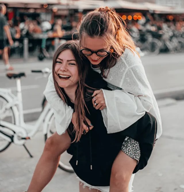 Two students piggyback riding outdoors exterior at Victory East Lansing in East Lansing Student Accommodation