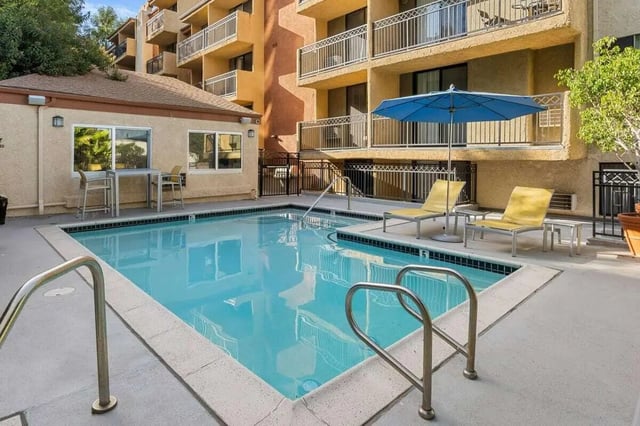 Pool with lounge chairs and blue umbrella recreation area at Ariel Court in Los Angeles Student Accommodation