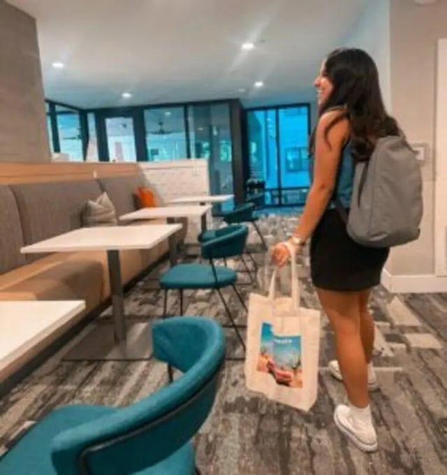 Banquette seating tables chairs with woman in backpack common area at Noble 2500 in Austin Student Accommodation