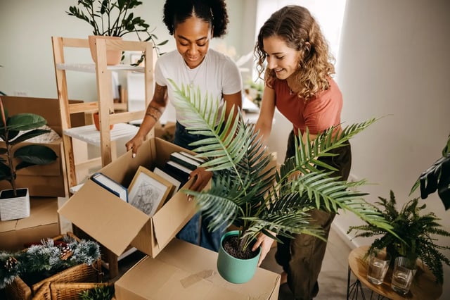 Two women unpacking boxes with plants and books living room at Campus Communities- Campus Creek Townhomes in Big Rapids Student Accommodation
