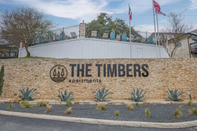 Stone wall with large text logo and landscaping exterior at The Timbers in San Marcos Student Accommodation