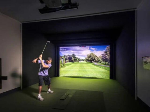 Man swings golf club on simulator screen Playing area at Brexx at Louisville in Louisville Student Accommodation
