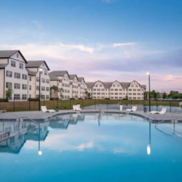 Apartment buildings by swimming pool with lounge chairs exterior at Bellamy Daytona in Daytona Beach Student Accommodation