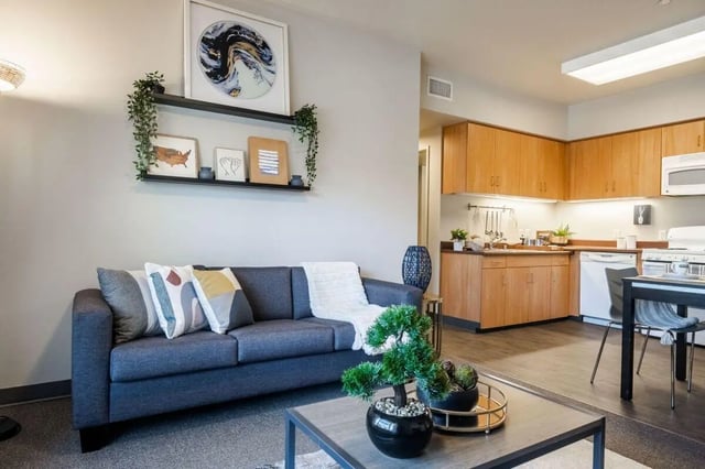 Sofa artwork shelves kitchen with wood cabinets living room at Claremont Collegiate Apartments