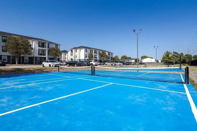 Blue court with tennis net and basketball hoop exterior at Crossing Place in College Station Student Accommodation